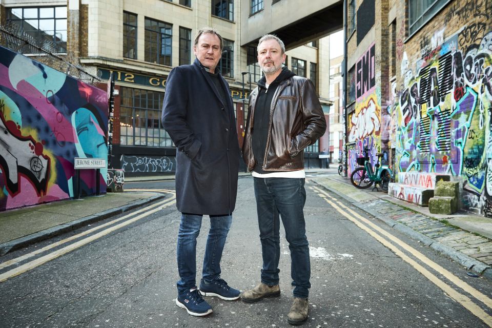 two men are standing in front of a graffiti covered wall with the number 12 on it