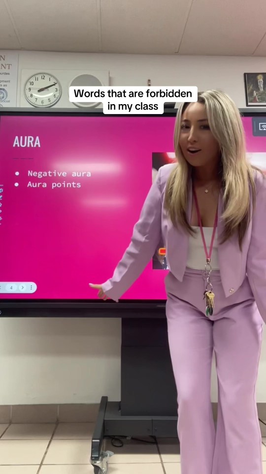 a woman in a purple suit stands in front of a pink board that says aura
