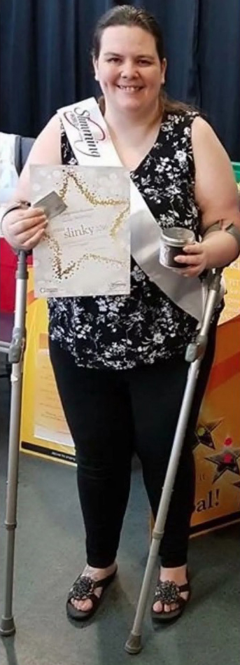 a woman with crutches is holding a certificate and smiling .