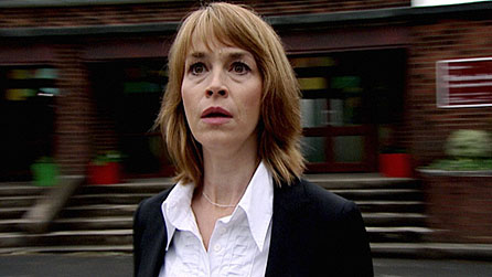 a woman in a suit and white shirt is standing in front of a brick building .