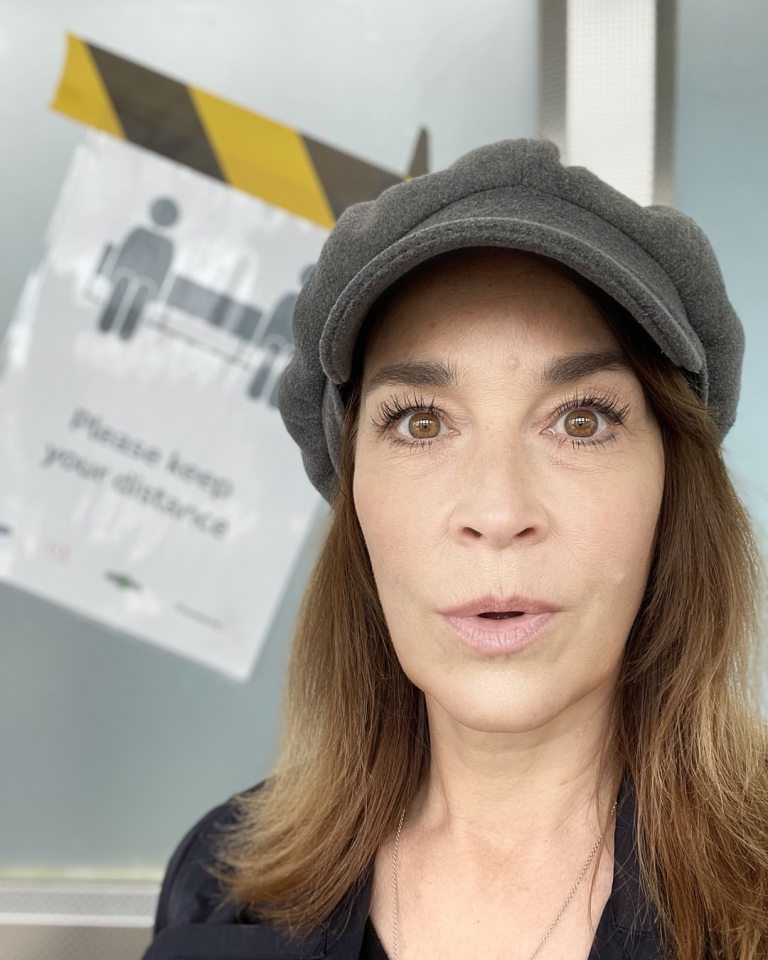 a woman wearing a hat stands in front of a sign that says please keep your distance