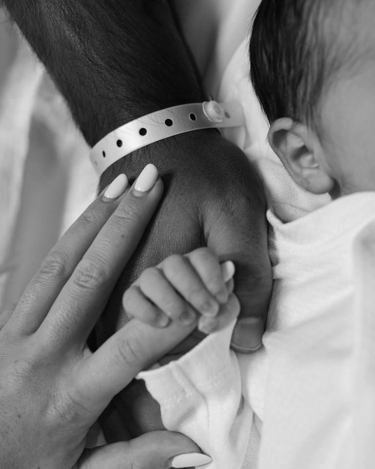 a black and white photo of a man and woman holding a baby 's hand