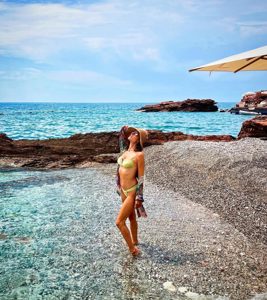 a woman in a bikini is standing on a rocky beach near the ocean