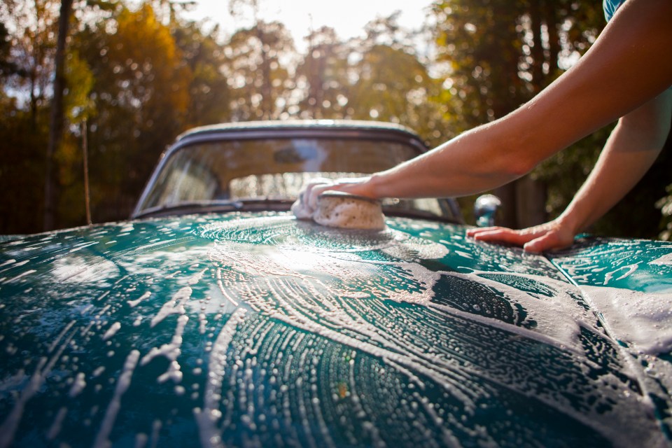 a person is washing a blue car with a sponge