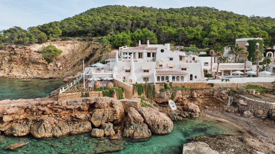 a large white house sits on a rocky cliff overlooking a body of water