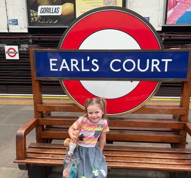 a little girl sitting on a bench under a sign that says earl 's court