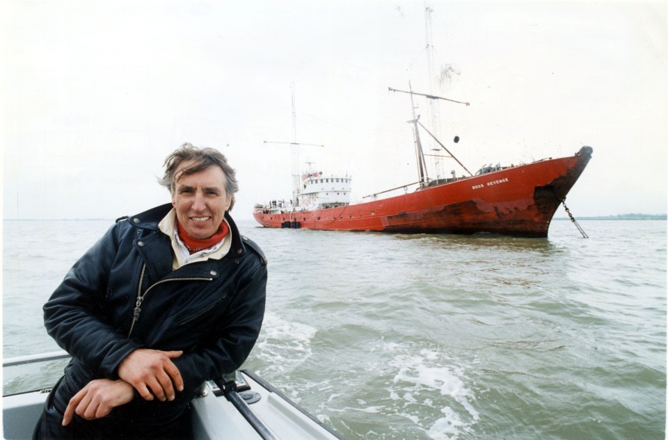 a man stands on a boat in front of a large red boat which says ross reservoir
