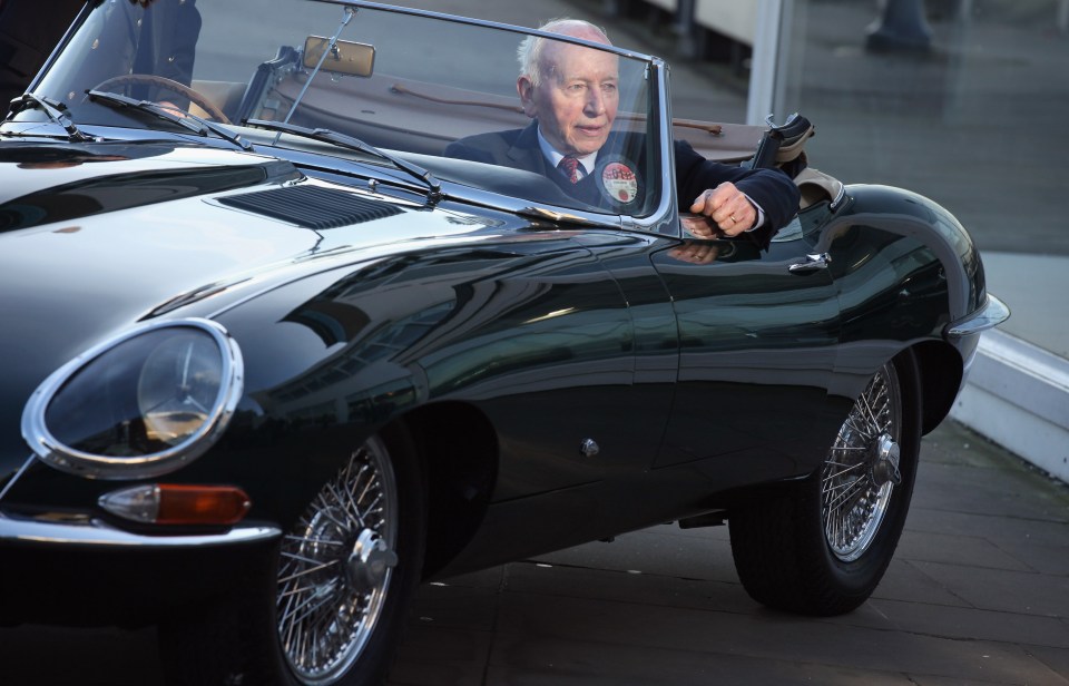 a man in a suit and tie is driving a black sports car