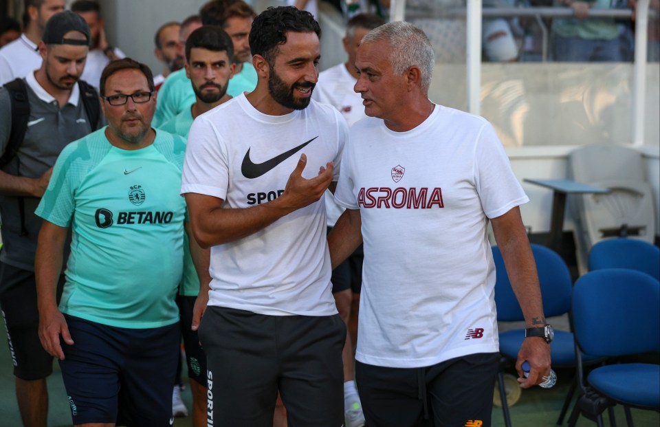 a man wearing a white asroma shirt talks to another man