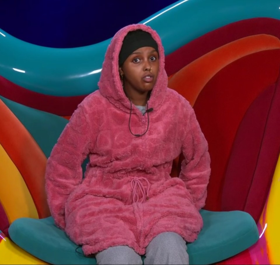 a woman in a pink hoodie sits in a colorful chair