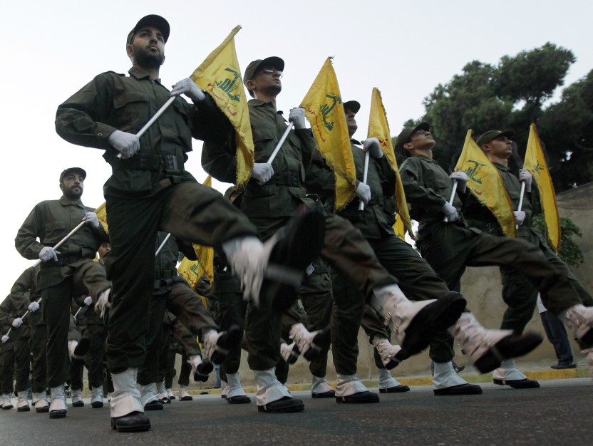 a group of soldiers marching in a line holding yellow flags with arabic writing on them