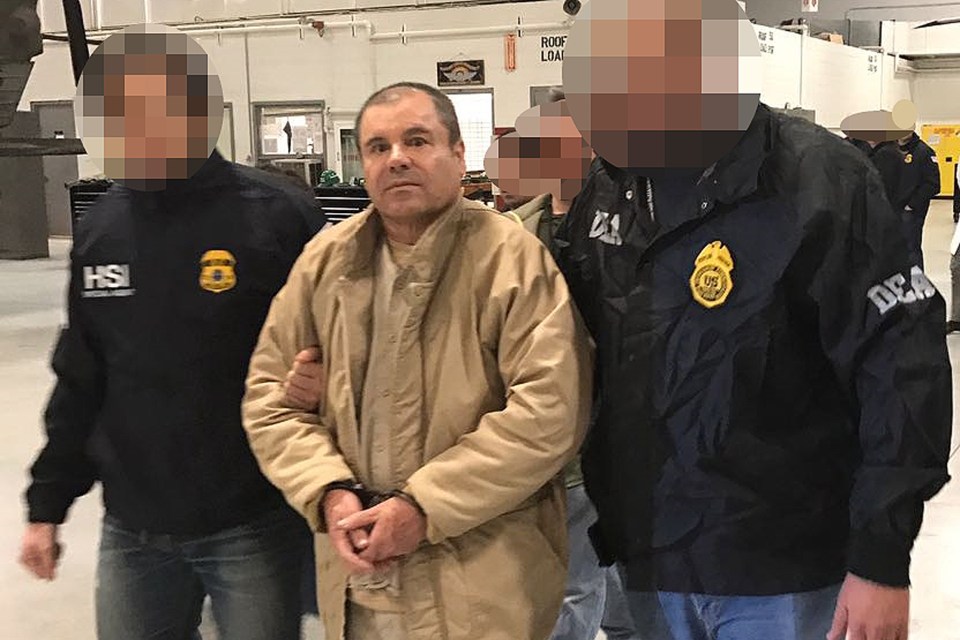 a man in a tan jacket is being escorted by two men in black jackets with the letters hsi on them