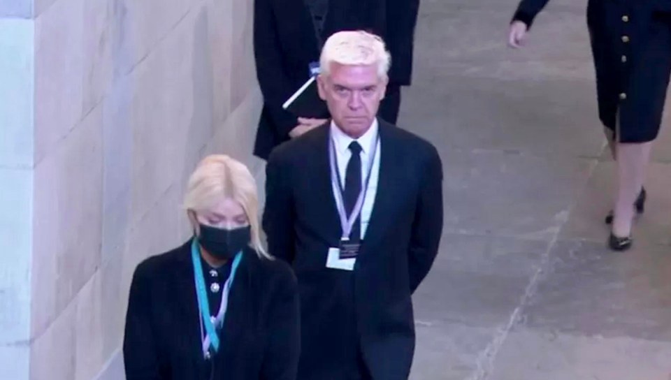 a man in a suit and tie is walking down a hallway next to a woman wearing a mask .