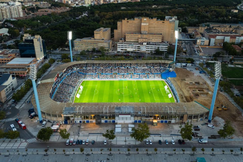 an aerial view of a soccer stadium with a large hospital in the background