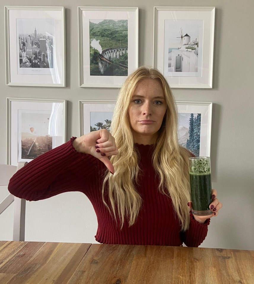 a woman sitting at a table holding a glass of green juice