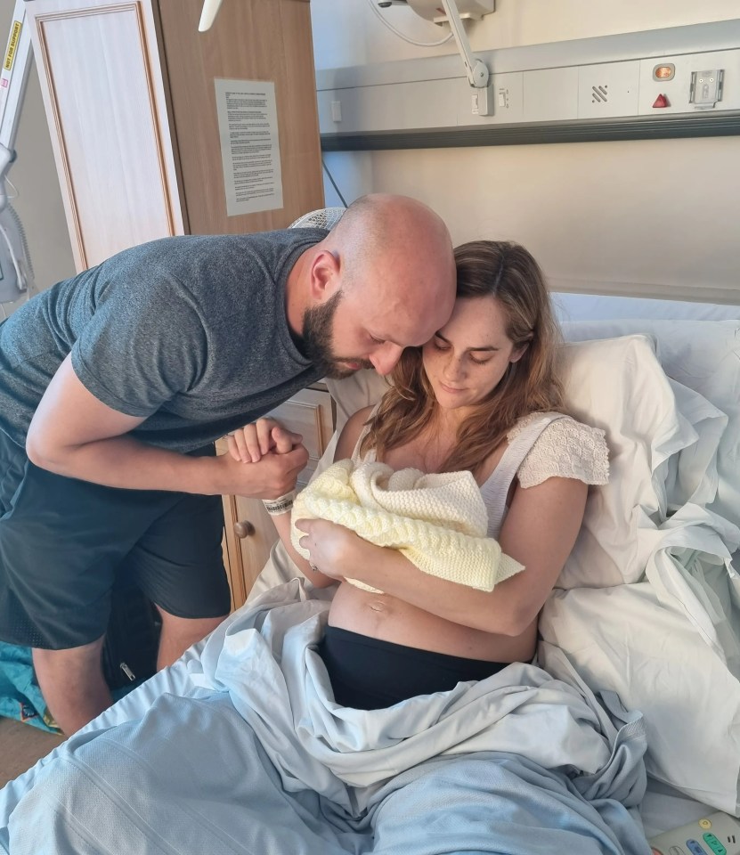 a man kisses a woman who is holding a baby in a hospital bed