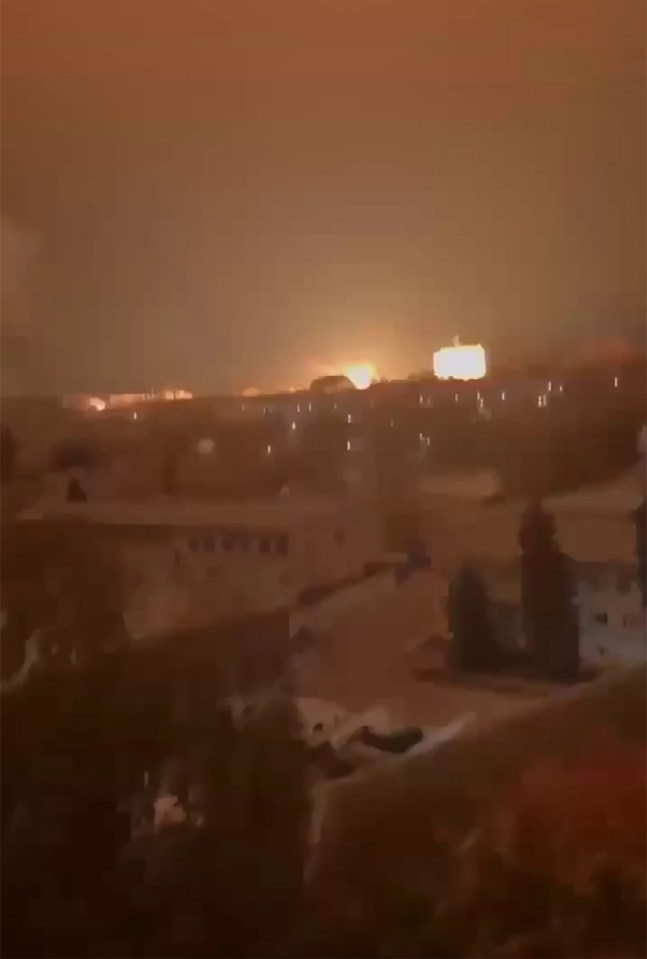 a group of people are sitting on a roof watching a fire in the sky .