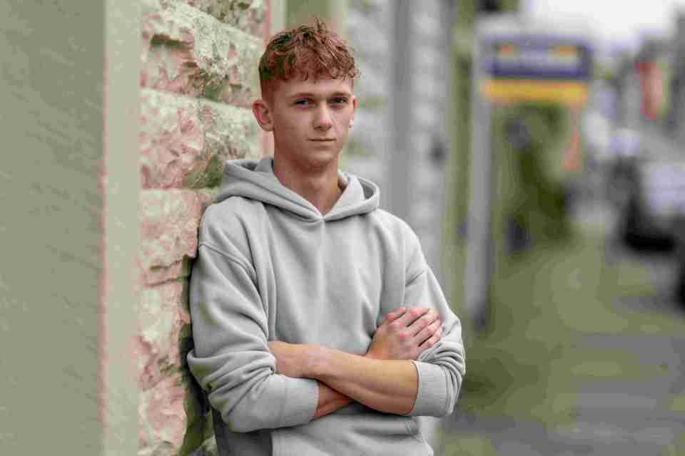 a young man leaning against a wall with his arms crossed