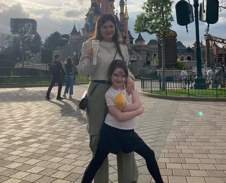 a woman holding a glass of champagne stands next to a little girl in front of a castle