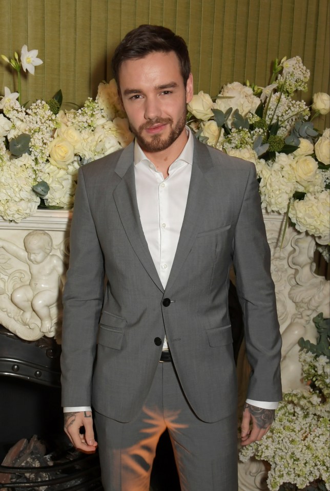 a man in a suit stands in front of a fireplace filled with white flowers