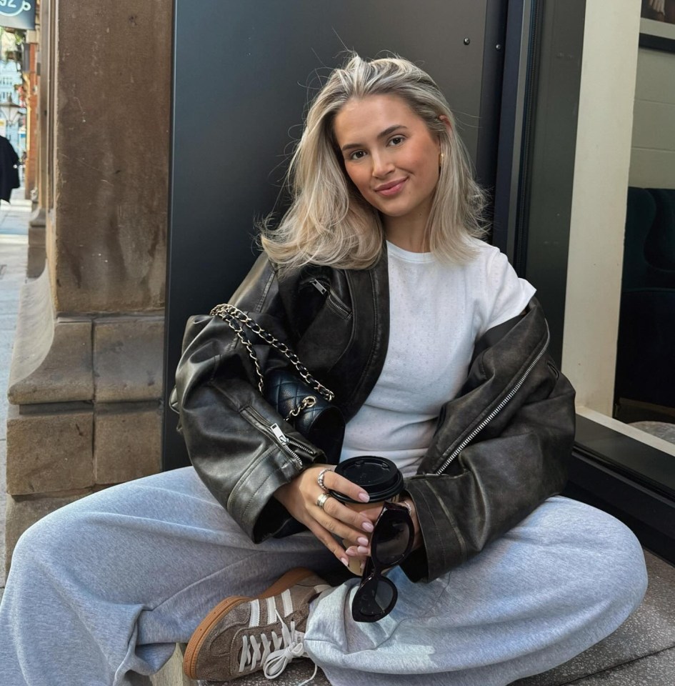 a woman in a leather jacket sits on the sidewalk holding a cup of coffee