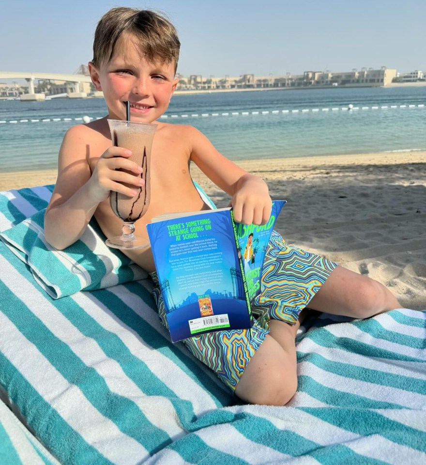 a young boy sits on a beach reading a book called the adventures of peter pan