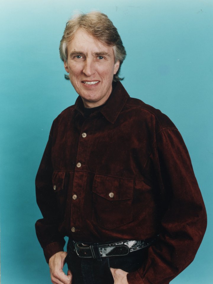 a man in a brown shirt is smiling with his hands in his pockets