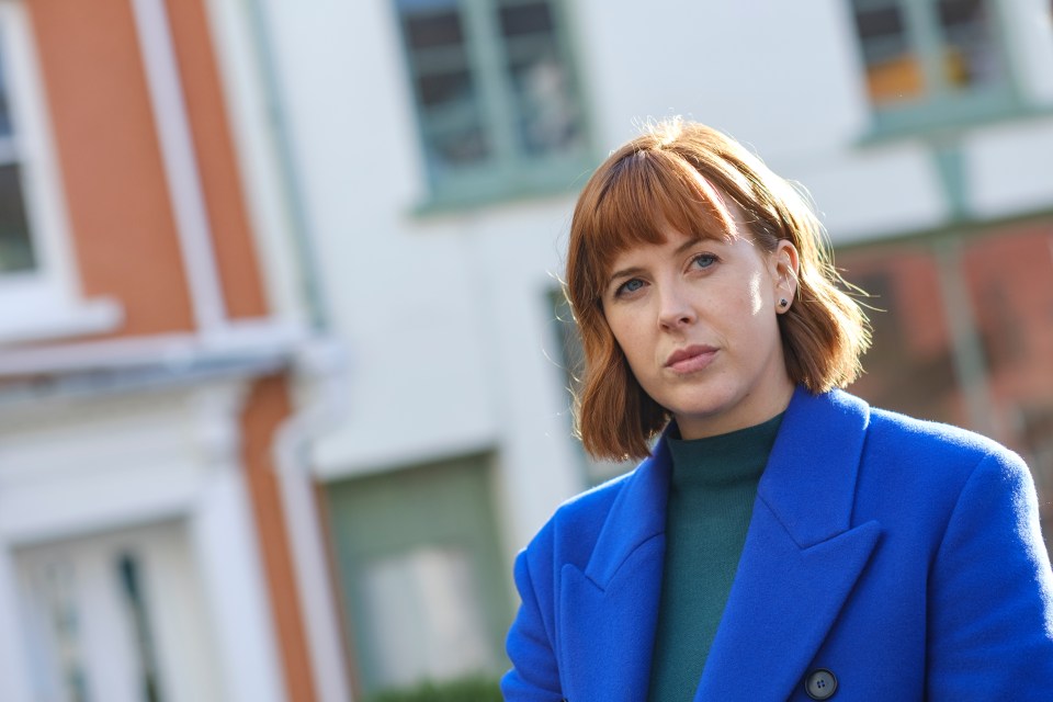 a woman in a blue coat stands in front of a building