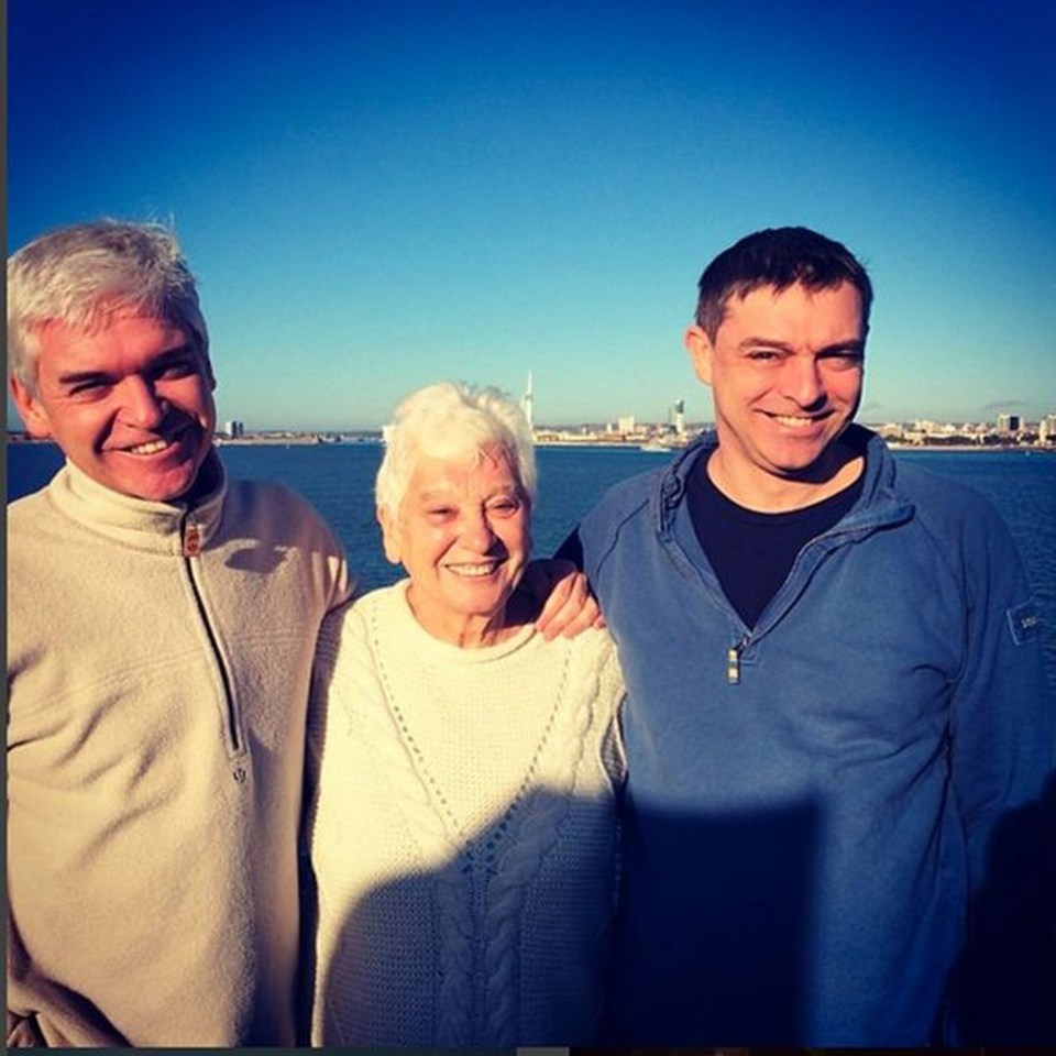 two men and an older woman pose for a picture in front of a body of water