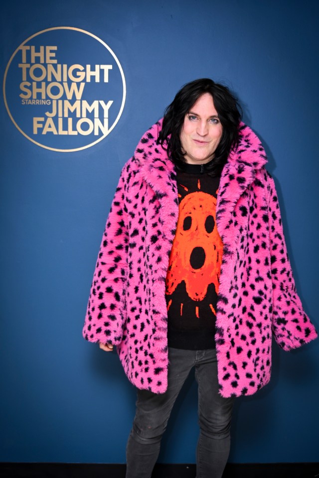 a man in a pink fur coat stands in front of a sign that says the tonight show jimmy fallon