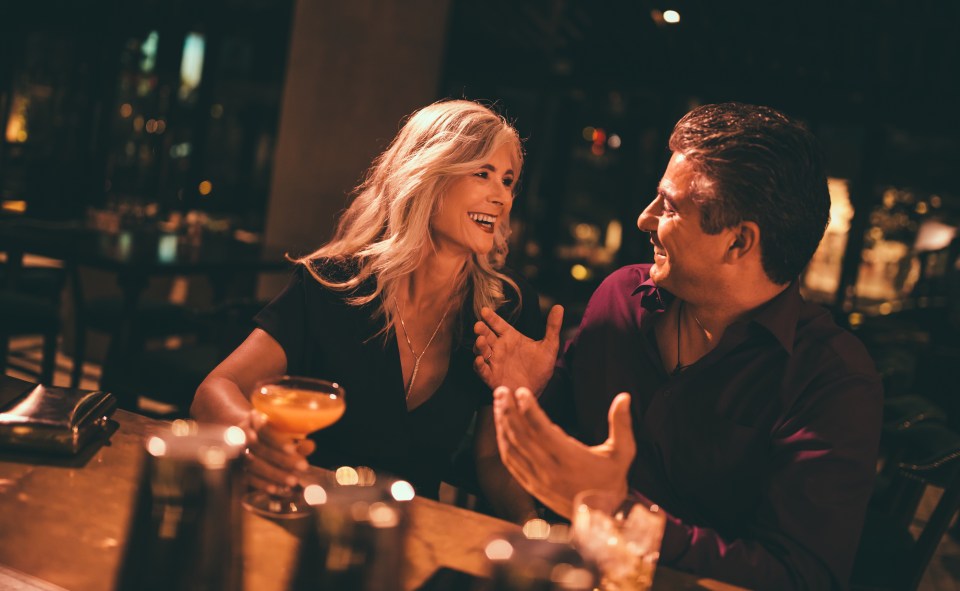 a man and a woman are sitting at a bar drinking cocktails