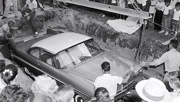 a black and white photo of a car being pulled out of a hole in the ground .