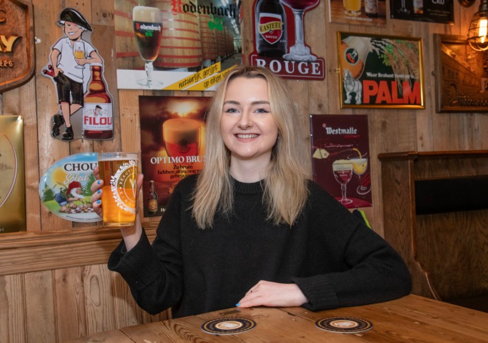 a woman holds a glass of beer in front of a sign that says palm