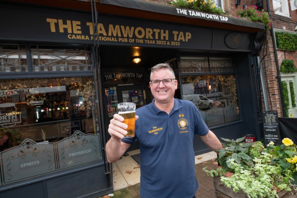 a man holds a glass of beer in front of the tamworth tap