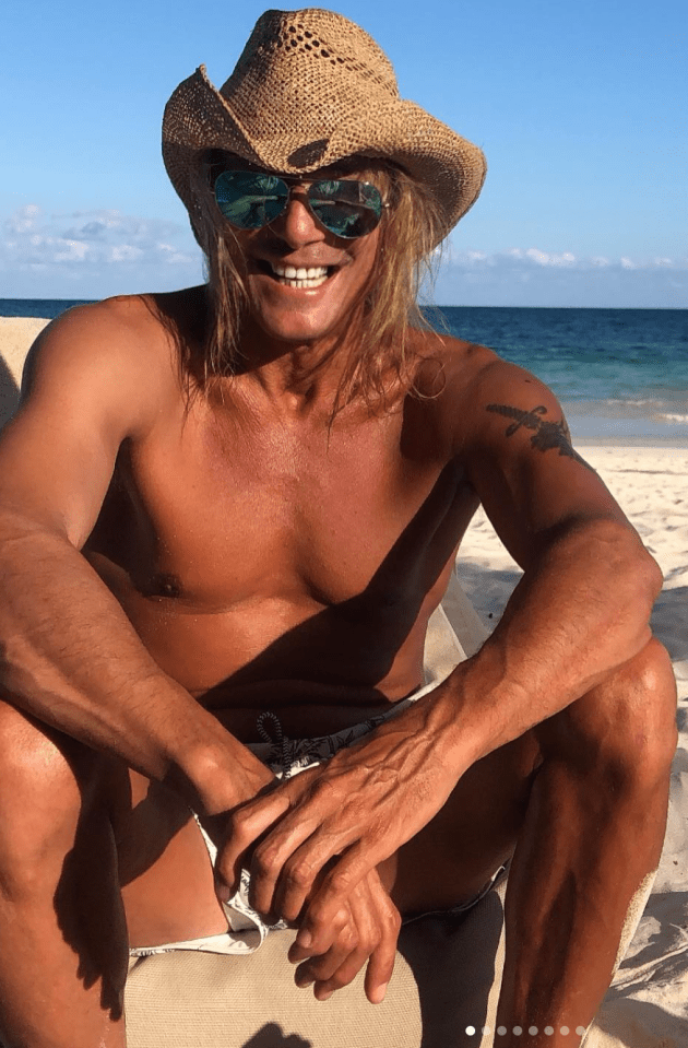 a shirtless man wearing a cowboy hat and sunglasses sits on the beach