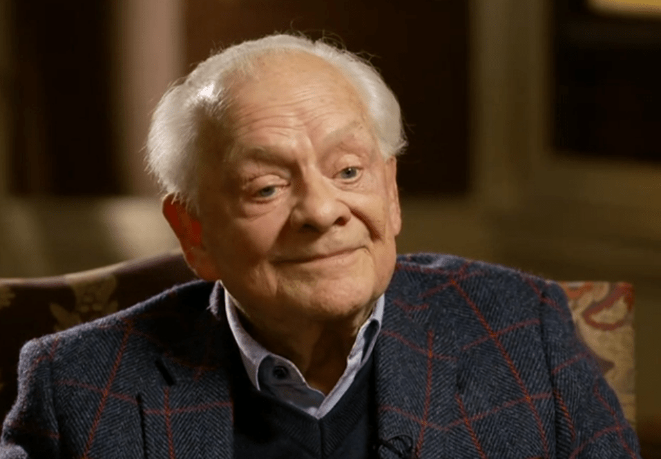 an older man in a plaid jacket sits in a chair