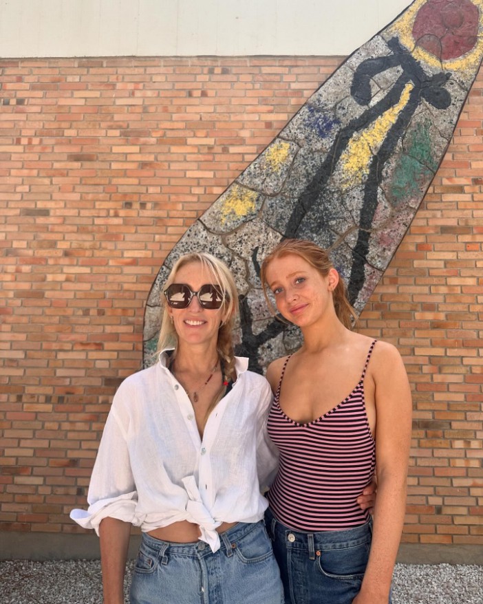 two women standing next to each other in front of a brick wall