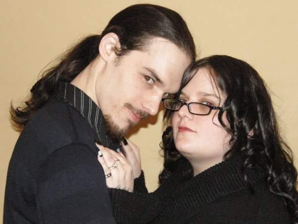 a man and a woman are posing for a picture together . the woman is wearing glasses and a ponytail .