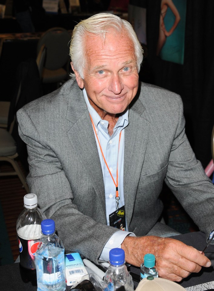 a man in a suit sits at a table with a pepsi bottle in front of him