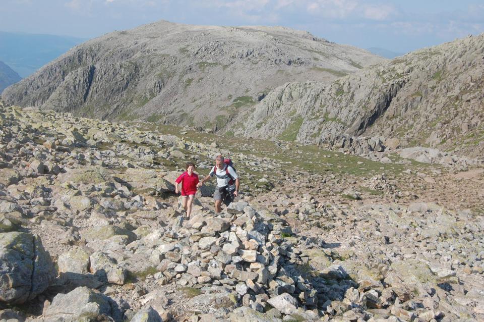 two people walking on a rocky hillside with a mountain in the background