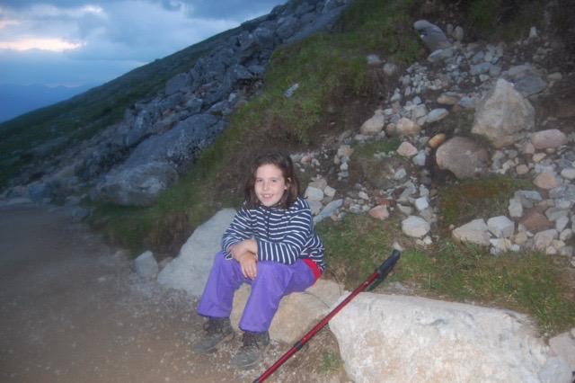 a young girl sits on a rock next to a hiking pole