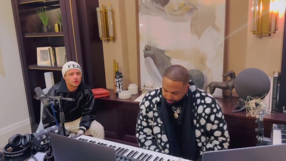 a man wearing a fed hat sits next to a man playing a keyboard