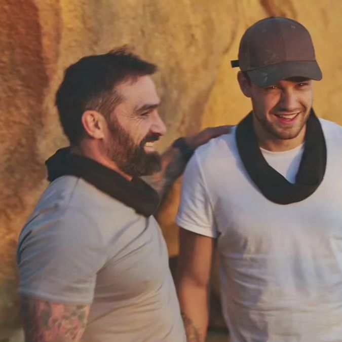 two men standing next to each other with one wearing a hat