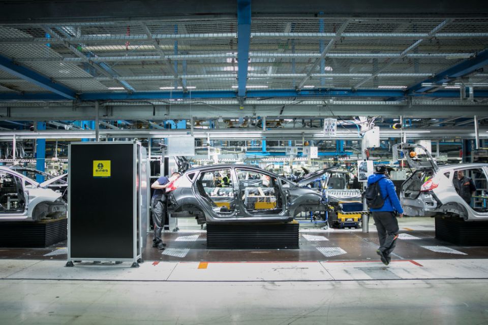 a man in a blue jacket walks through a car factory