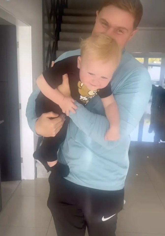 a man is holding a baby in his arms and the time is 12h
