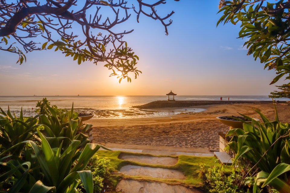 a sunset over a beach with a gazebo in the distance