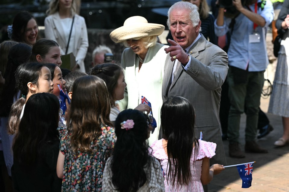 a man in a suit and a woman in a hat are talking to a group of children