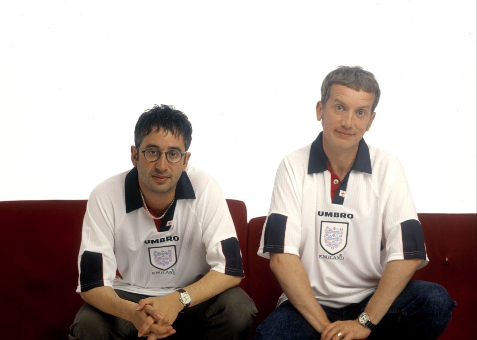 two men wearing umbro england shirts sit on a red couch