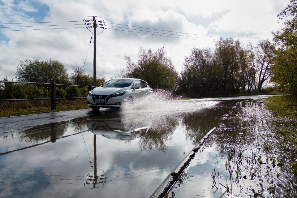 a white nissan car drives through a puddle of water
