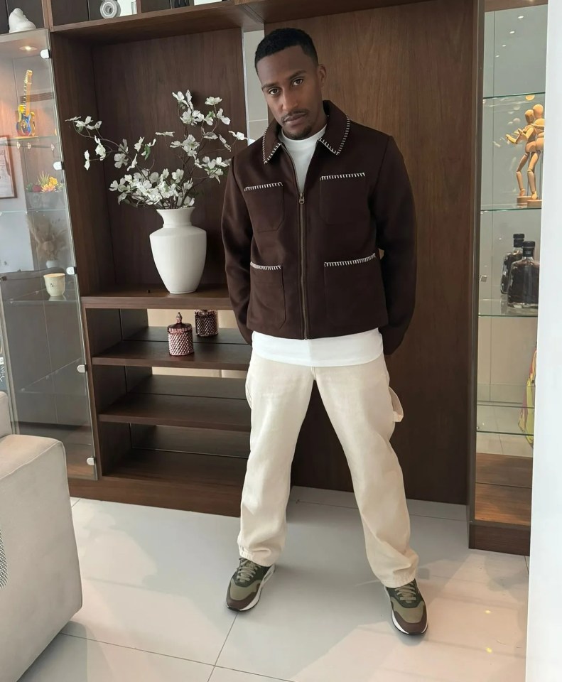 a man in a brown jacket stands in a living room